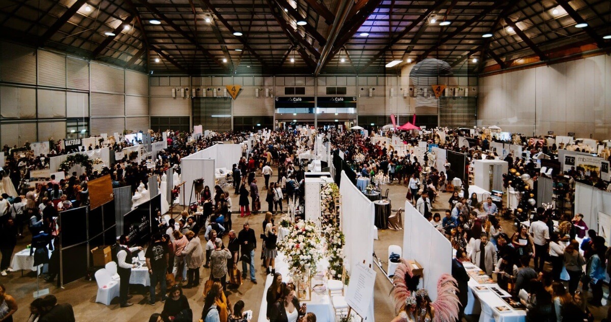 The image shows a large, crowded wedding expo.