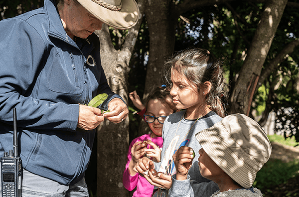 Park ranger with sunhat and radio, interacting with three young people in the Park.